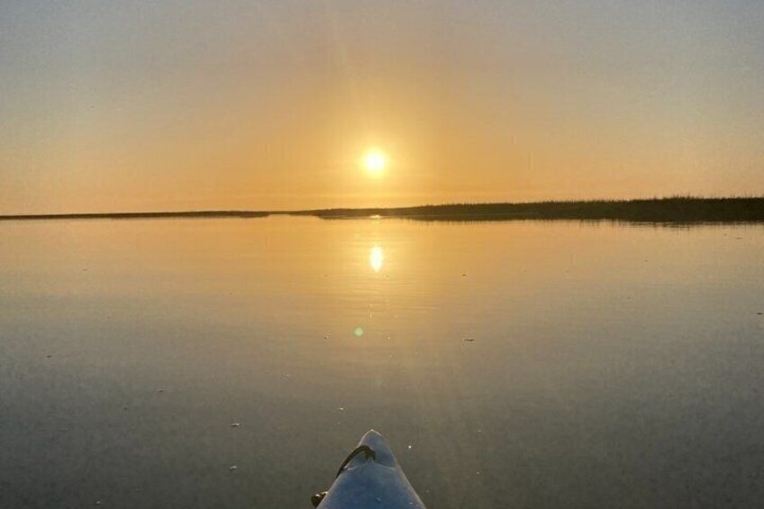 A calm body of water reflecting the sun, a clear sky, and a distant shoreline. 2