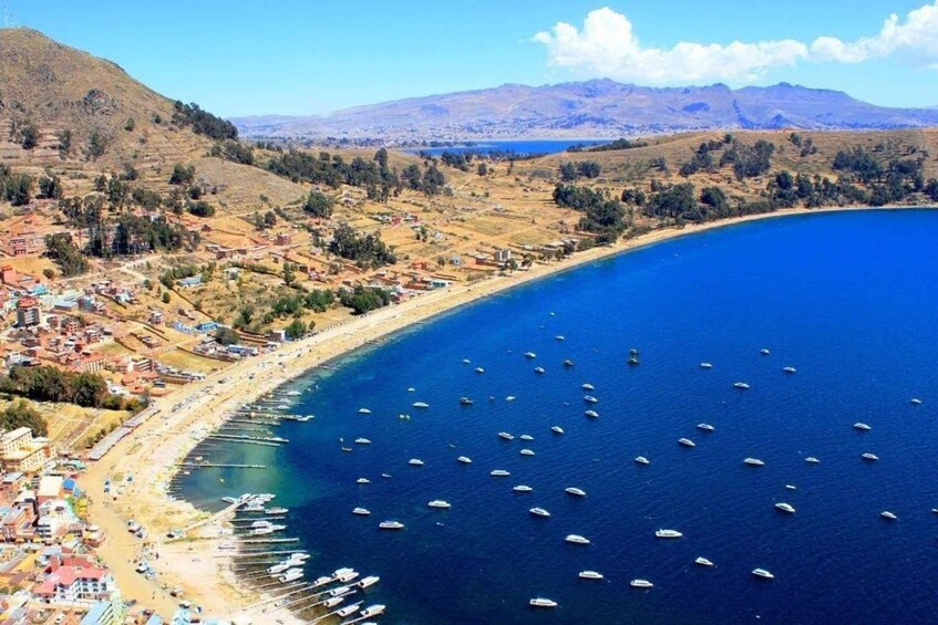 A coastal town with boats docked along the shoreline, a beach, and hills in the background. 1
