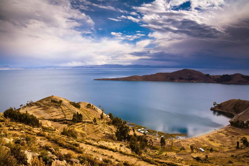 A coastal landscape with rolling hills, a calm sea, and a partly cloudy sky. 4