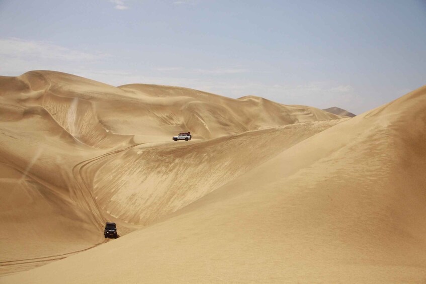 A desert landscape with sand dunes and vehicles navigating the terrain. 5