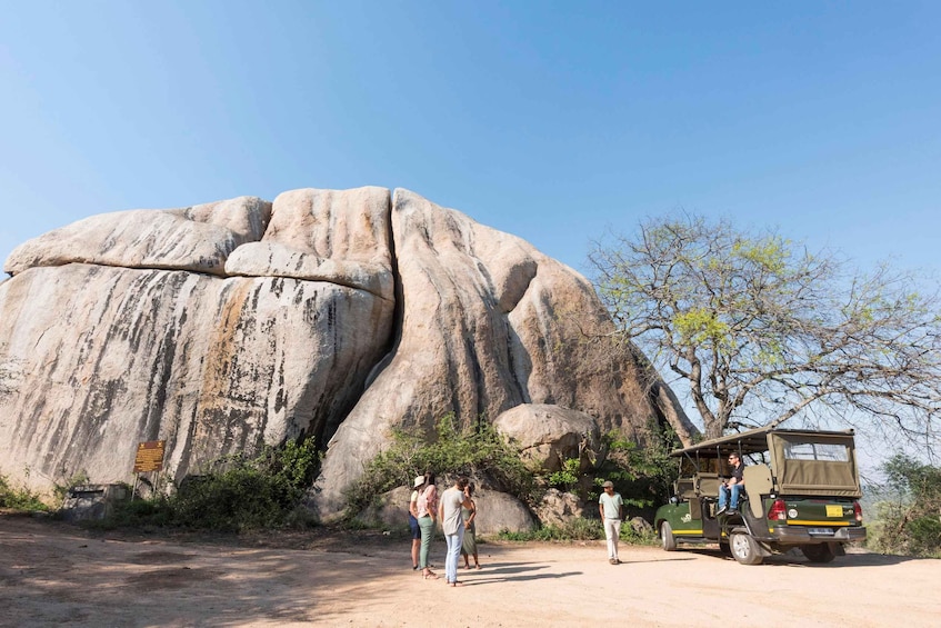 A large rock formation, a group of people, and a safari vehicle. 4