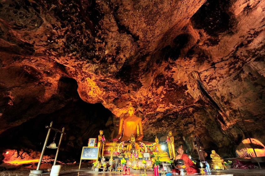 A large Buddha statue in a cave with smaller statues and offerings. 4