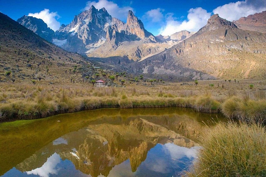 A mountain landscape with a reflective pond, a small building, and a clear sky. 2