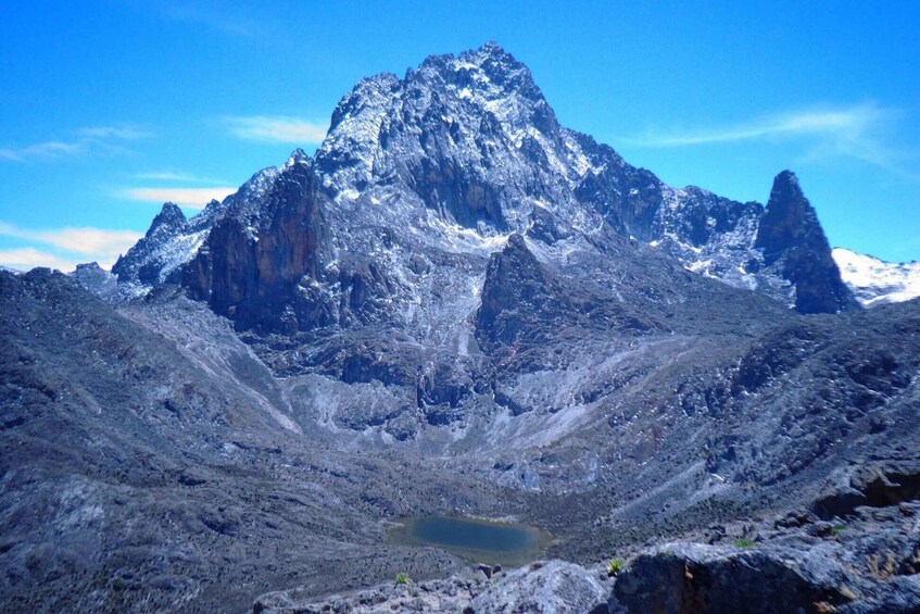 A rugged mountain range with a prominent peak and a small lake at its base. 3