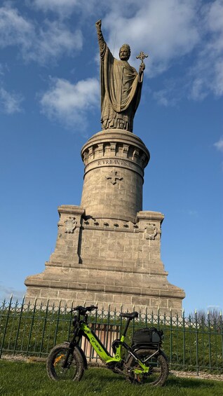 A statue with a raised arm and a cross, a green bicycle, and a fence in the foreground. 4