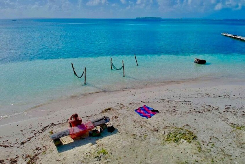 A beach with clear turquoise water, a hammock, and a colorful blanket. 1