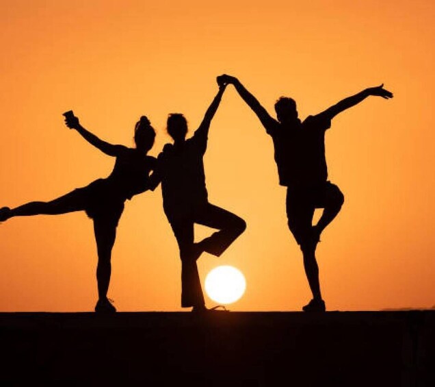 Three silhouetted figures performing a dance against a sunset. 5