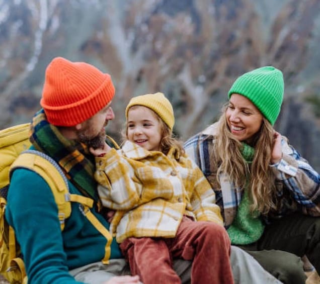 A family with a child, wearing winter hats and jackets, sitting outdoors. 1