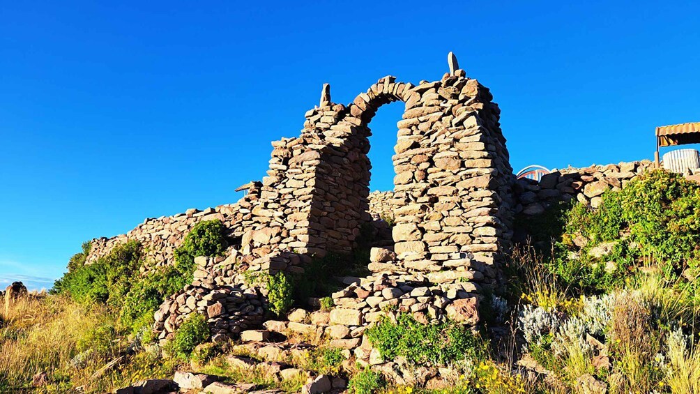 Ancient stone ruins with a large archway, surrounded by greenery and a clear blue sky. 3