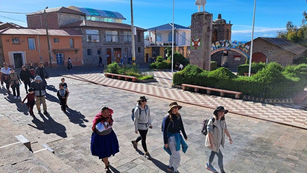 A historical square with people walking, a statue, and traditional buildings. 2