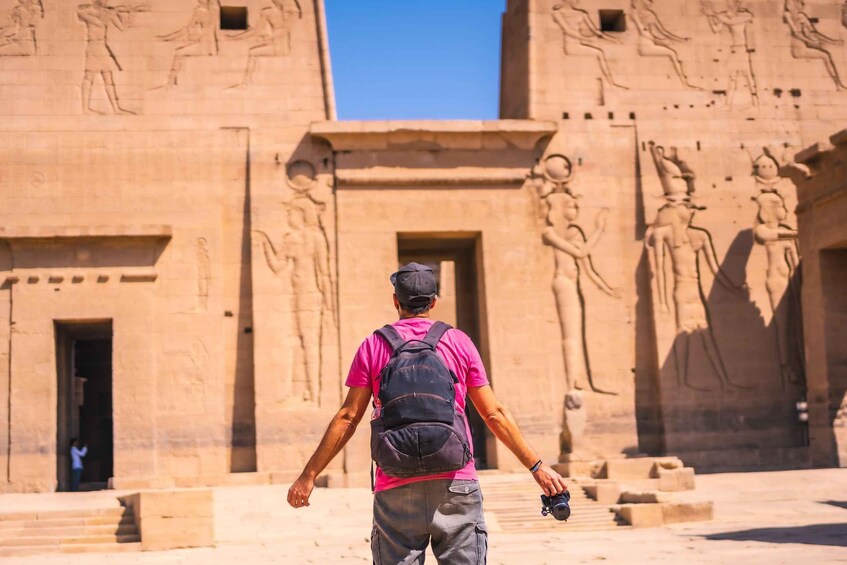 A person with a backpack and camera in front of an ancient Egyptian temple with hieroglyphs. 3
