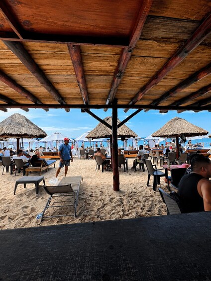 A beach with wooden structures, thatched umbrellas, and lounge chairs. 3