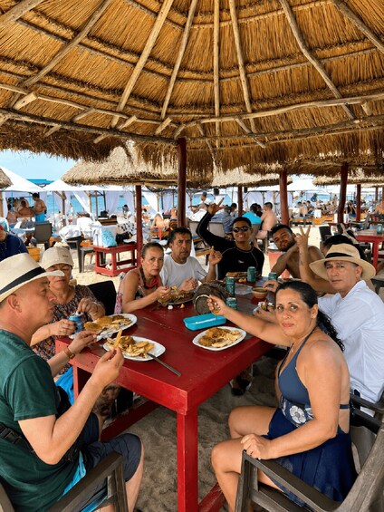 A group of people dining at a beachside restaurant with a thatched roof. 4