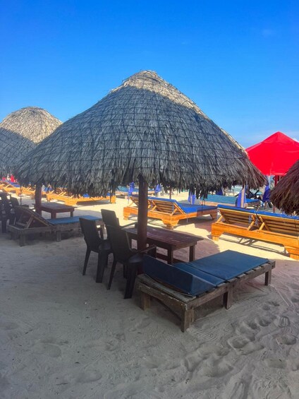 A beach with thatched umbrellas, wooden lounge chairs, and a red tent. 5
