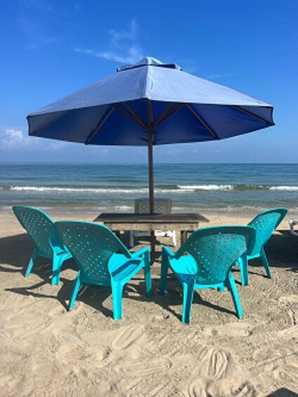 A beach with turquoise chairs and a table under a blue umbrella. 4