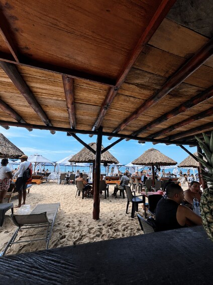 A beach with wooden structures, tables, and chairs under a thatched roof. 2