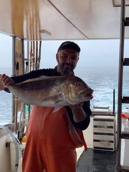 A person holding a large fish on a boat with the ocean in the background. 1