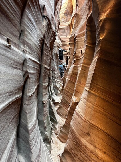 A narrow canyon with layered rock formations and a person climbing. 1