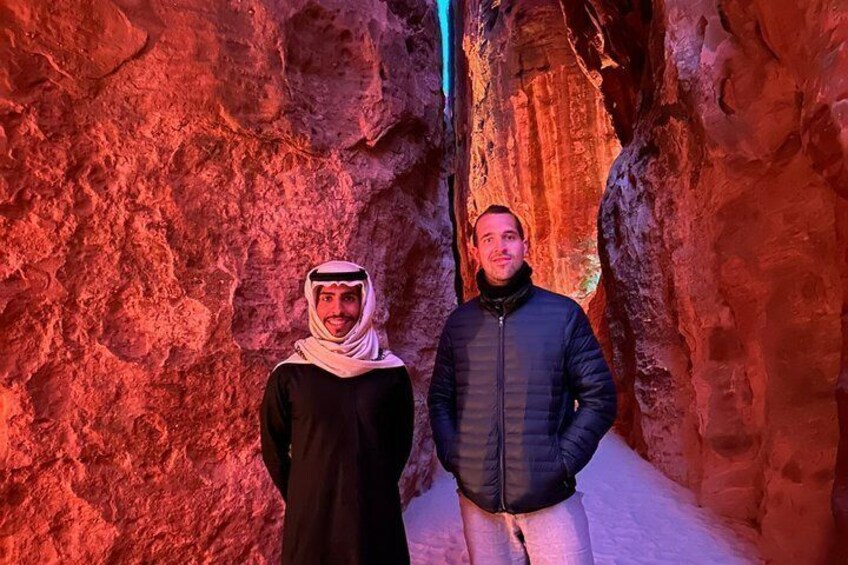 Two people standing in a narrow, rocky passageway with red lighting. 1