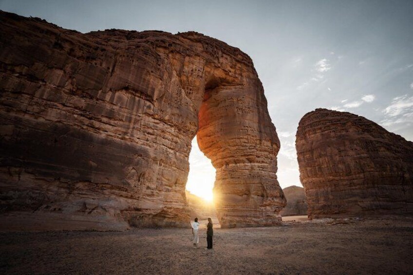 A person standing in front of a rock formation with a sun setting behind it. 2