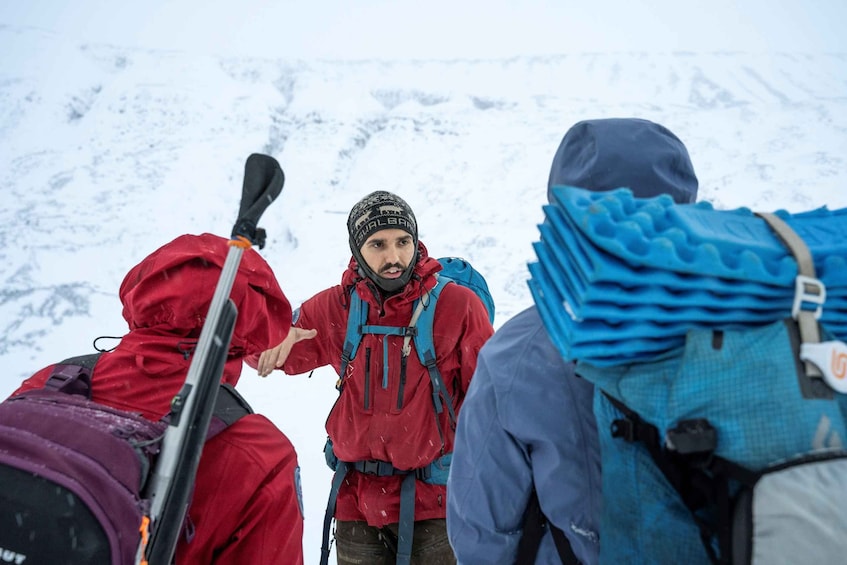 A group of hikers with backpacks and skis in a snowy mountainous area. 4