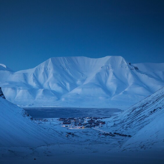 A snow-covered mountain range with a small settlement at its base. 2