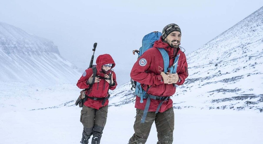 Two hikers in red jackets with backpacks on a snowy mountain trail. 5