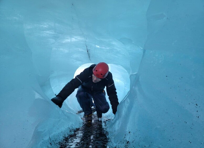 A person in a red helmet and black jacket navigating through a narrow, icy tunnel. 2