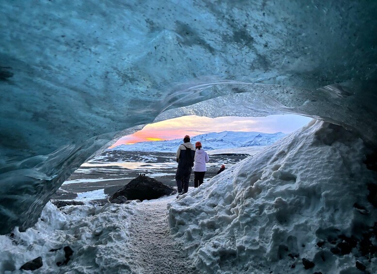 An ice cave with a view of a sunset over snow-covered mountains. 1