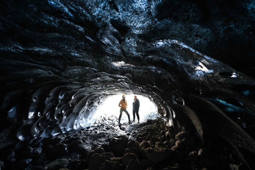 Two people standing inside a cave with ice formations. 3