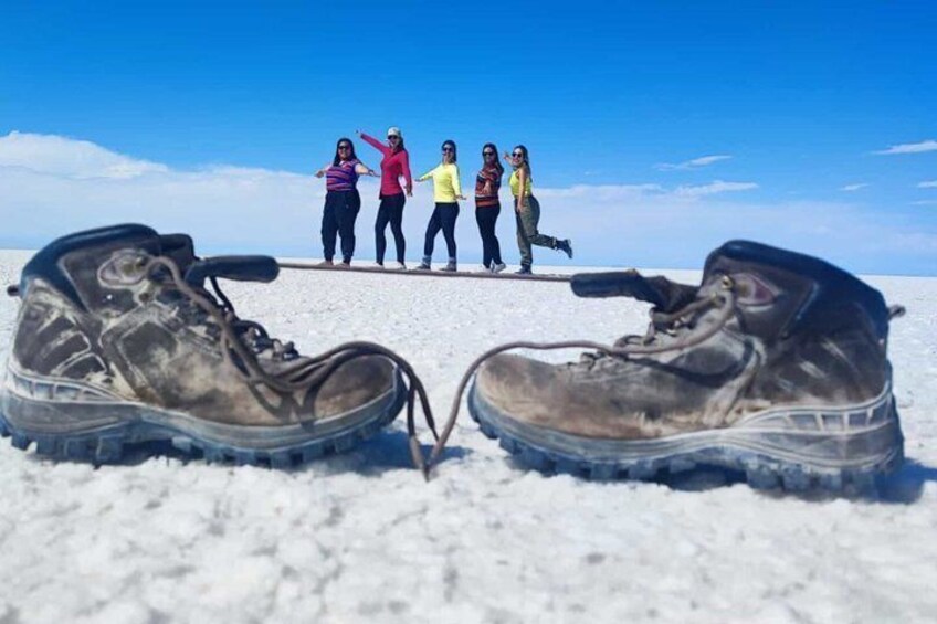 A pair of hiking boots in the foreground with a group of people standing in the background on a snowy landscape. 3