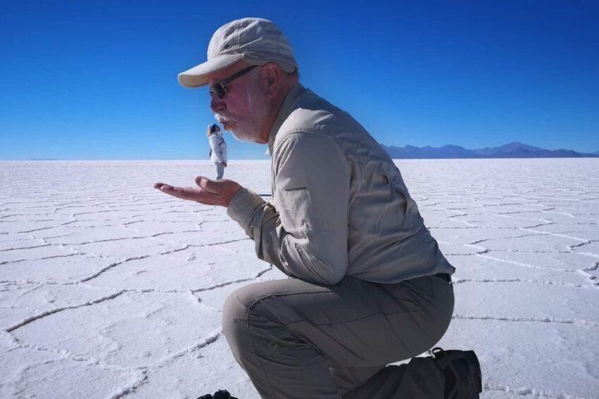 A person crouching in a vast salt flat with a clear sky and distant mountains. 1