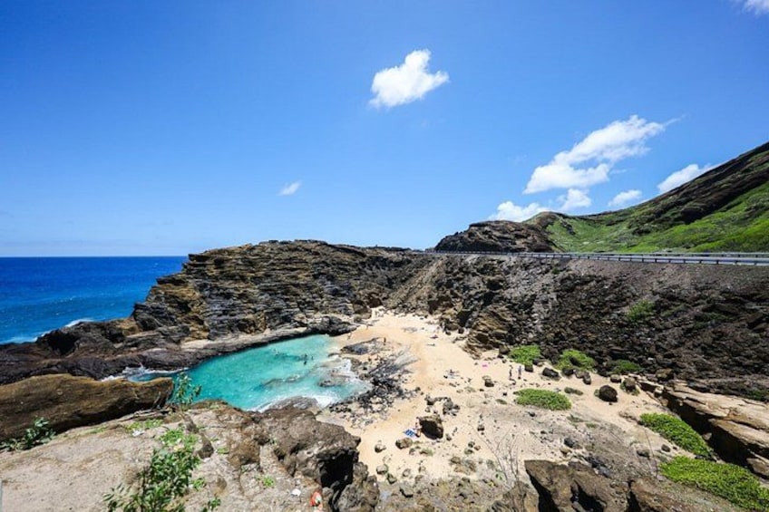 A coastal landscape with a clear blue sea, rocky cliffs, and a sandy beach. 4