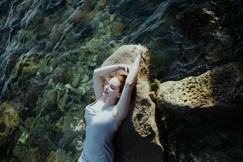 A person leaning on a rock by a clear body of water. 1
