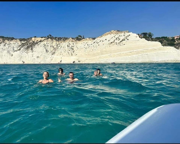 A group of people swimming in clear blue water with white cliffs in the background. 3