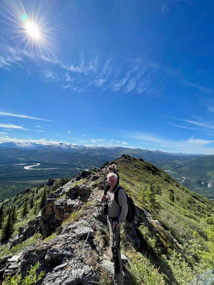 A hiker on a mountain trail with a clear sky and distant snow-capped peaks. 1