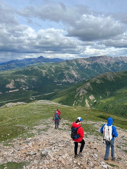 Hikers on a rocky mountain trail with a view of distant mountains and a cloudy sky. 2
