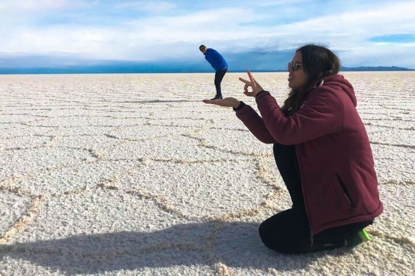 A person kneeling on a salt flat with a person standing on a rock in the distance. 1