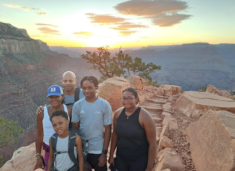 A group of people standing on a rocky outcrop with a canyon and sunset in the background. 1