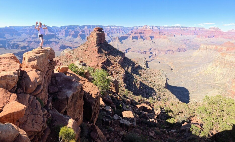 A person standing on a rock formation with a view of the Grand Canyon in the background. 2