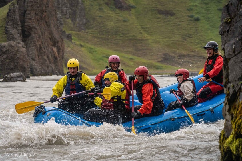 A group of people in a blue raft navigating a river with rapids, surrounded by rocky cliffs and greenery. 1