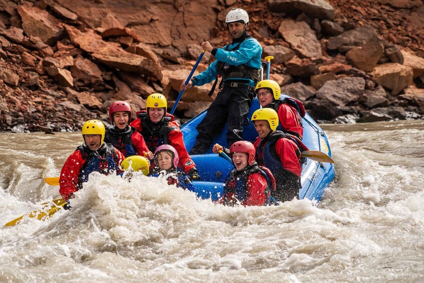 A group of people in a blue raft navigating through a river with white water rapids. 1