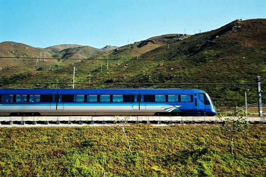 A blue train on tracks with a mountainous landscape in the background. 1
