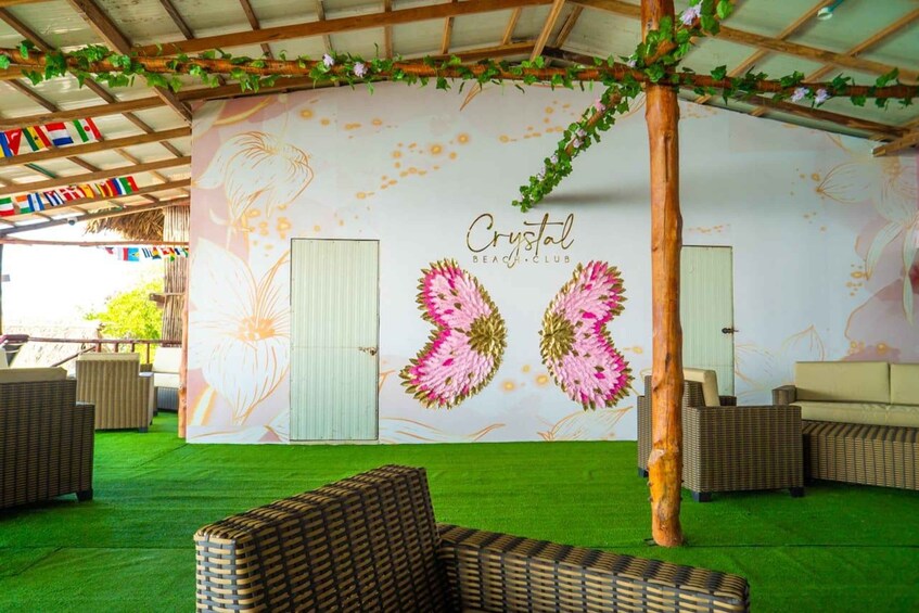 A beach club interior with wicker furniture, green artificial grass, and floral wall art. 1