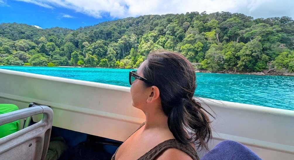 A person on a boat with turquoise water and a forested hill in the background. 3