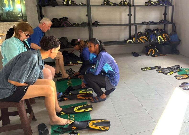 People sitting on the floor, wearing fins, and surrounded by diving gear. 5