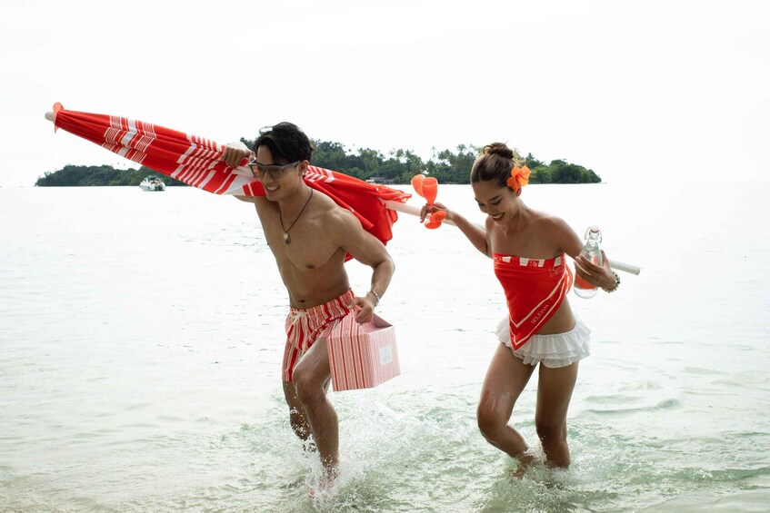 Two people in a body of water, one carrying a striped umbrella and the other holding a bottle. 4