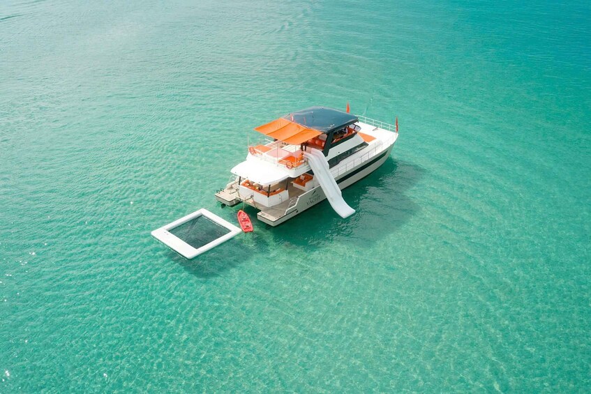 A white yacht with an orange canopy and a small dock extending into clear turquoise water. 3