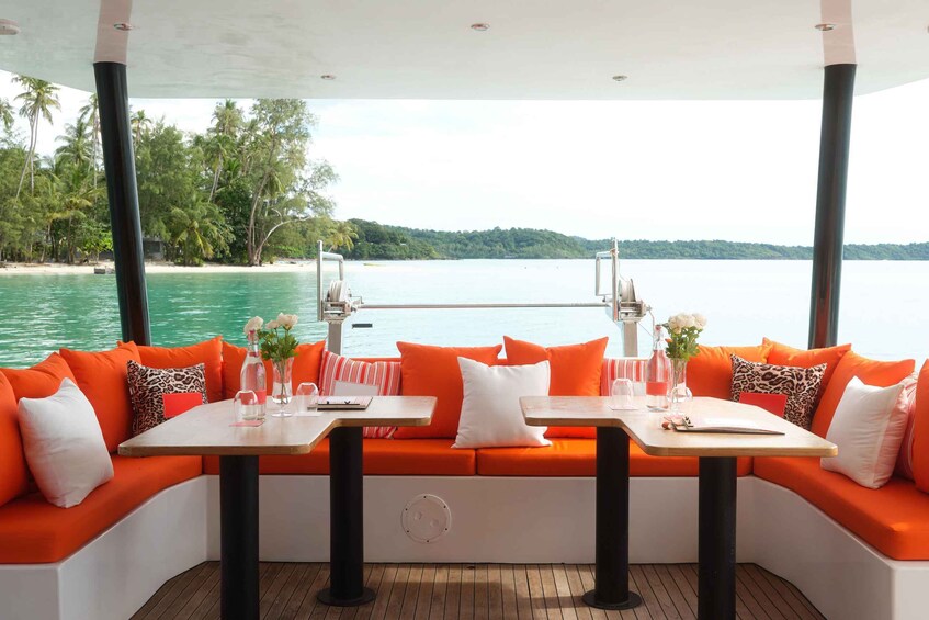 A boat deck with orange seating, white cushions, and a table set with glasses and flowers. 2