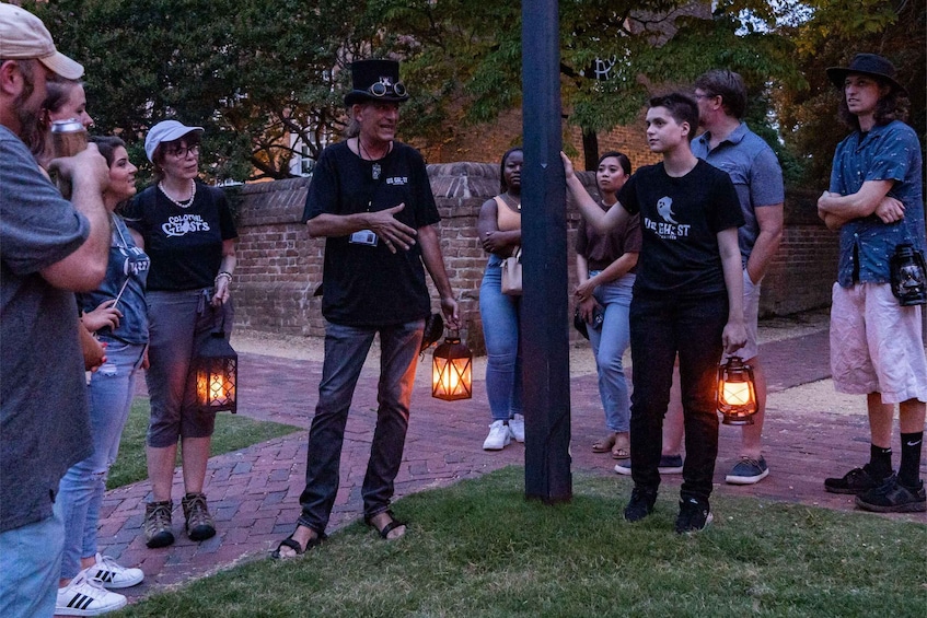 A group of people standing outdoors, some holding lanterns, in a park-like setting with brick pathways and trees in the background. 4
